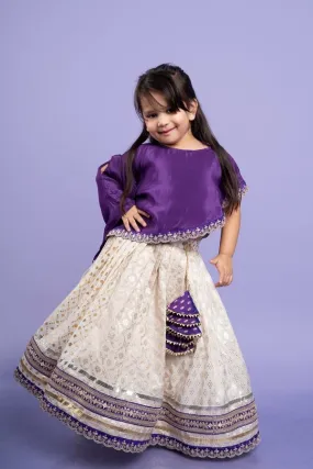 Elegant purple cape-style top with golden embroidery paired with a white lehenga adorned with delicate golden motifs and a broad purple and gold border.